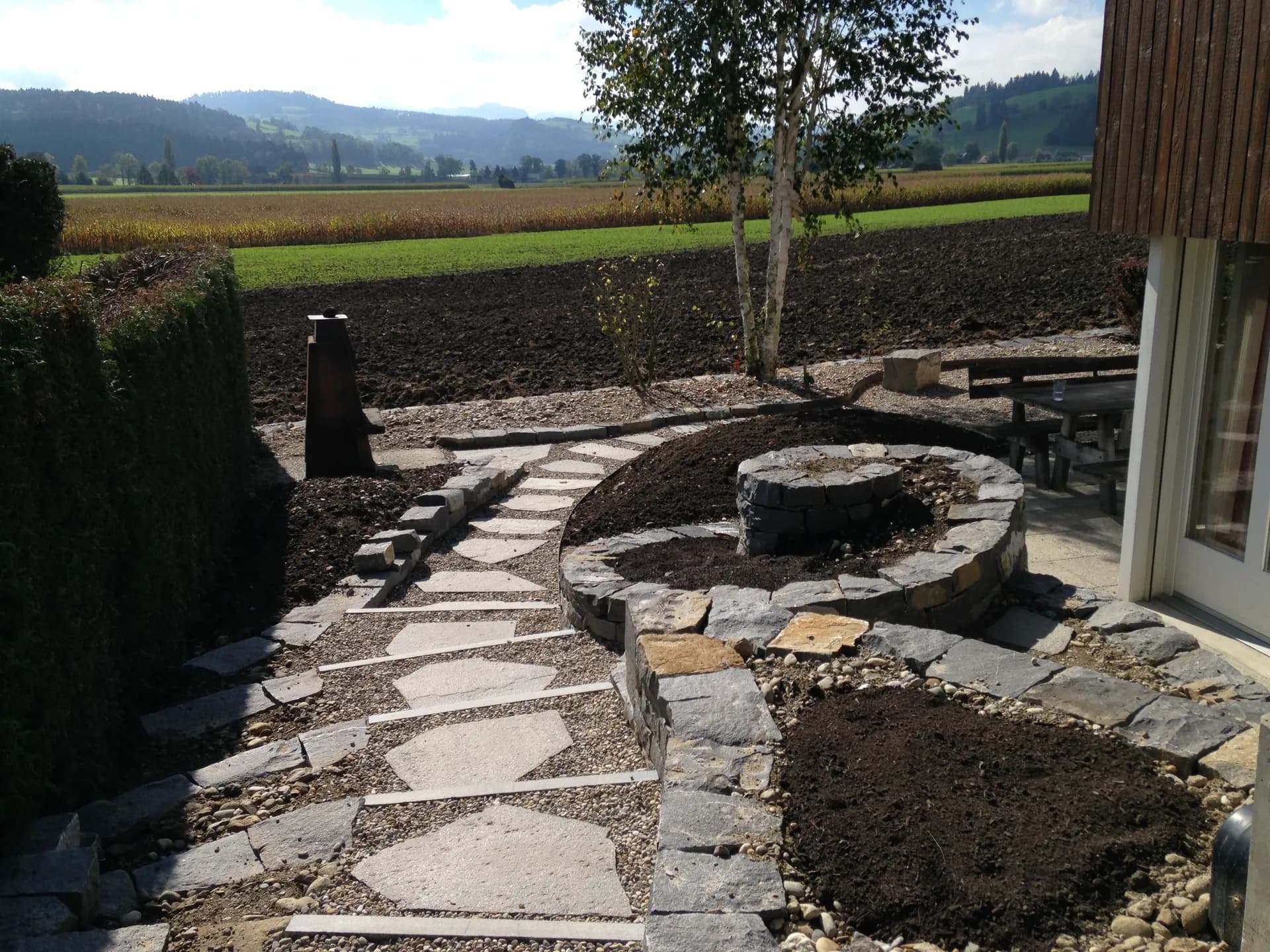 Trockensteinmauer-Rundbeet mit Natursteinplattenweg